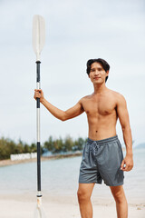 Wall Mural - Active Asian Man Paddleboarding for Summer Fun and Adventure at Sunset on a Beach