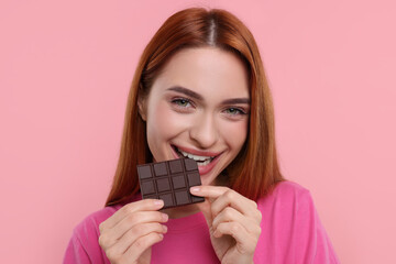 Young woman eating tasty chocolate on pink background