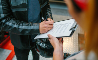 Unrecognizable biker man wearing leather jacket and holding helmet signing insurance policy to receipt his repaired motorcycle on workshop