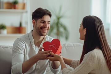 Wall Mural - a man giving gift box heart shape to his girl friend at home, light white room, 