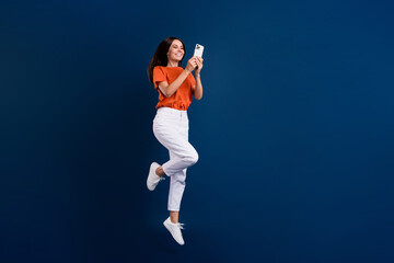 Poster - Full length photo of shiny cheerful lady wear orange t-shirt jumping chatting modern device empty space isolated dark blue color background