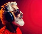 Fototapeta Sport - Elderly man listening to music in headphones on a red background. Music Streaming Service Concept with Copy Space.