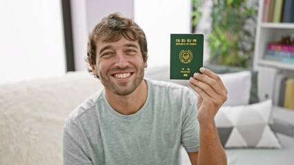 Sticker - Young man sitting on sofa holding passport of korea smiling at home