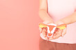 Female reproductive health concept. Woman hand holding uterus shape made from paper on pink background. Awareness of uterus illness such as endometriosis, PCOS, STDs, HPV or gynecologic cancer.