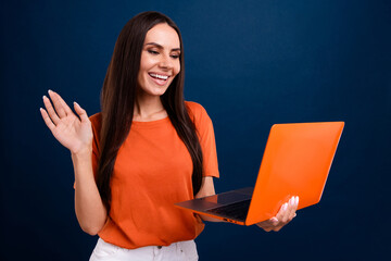 Poster - Photo of cheerful friendly lady wear orange t-shirt waving arm hi talking modern gadget isolated dark blue color background