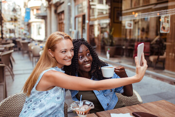 Wall Mural - Two young women taking selfie in street cafe