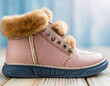 Pink leather warm child boots with fluffy fur, shoelaces and zipper on light wooden floor background. Closeup. Side front view. Empty place for text.