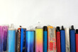 Multi-coloured discarded electronic cigarette vapes lined up on a white paper background. These are vapes that were found discarded on roads and pavements.