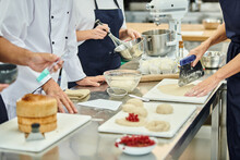 cropped view of hard working chefs and chief cook working with dough on kitchen, confectionery