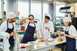 © LIGHTFIELD STUDIOS - mature chief cook in white hat explaining how to bake to his multicultural hard working chefs