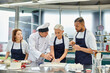 © LIGHTFIELD STUDIOS - good looking mature chief cook helping his multicultural chefs with pastries, confectionary