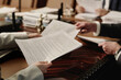 © AnnaStills - Two unrecognizable caucasian business people exchanging documents sitting at wooden desk in office