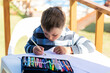 Boy about to draw on a blank paper with graphite pencil. He is outdoors sitting at a table.