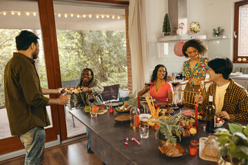 Wall Mural - Group of Happy friends enjoying in conversation and drinking wine during Christmas party at home