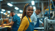 young woman smiling at the camera, wearing a yellow shirt and blue apron, in a manufacturing setting