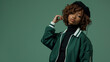 © Studio Nova - stylish woman posing confidently with her hand on her hat, wearing a green jacket with white details, against a matching green background