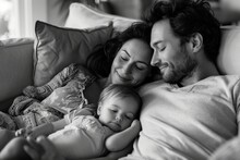 A Peaceful Moment Of Parenthood Captured As A Man And Woman Cradle Their Newborn Baby Boy In The Comfort Of Their Bedroom, All Three Faces Relaxed In The Blissful State Of Sleep. Black And White