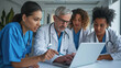© MP Studio - Focused group of medical professionals, including three doctors and nurses, gathered around a laptop, discussing or reviewing something of importance.