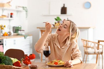 Wall Mural - Young woman eating tasty pasta in kitchen