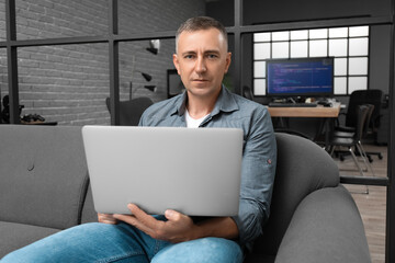 Wall Mural - Mature male programmer with modern laptop sitting on sofa in office