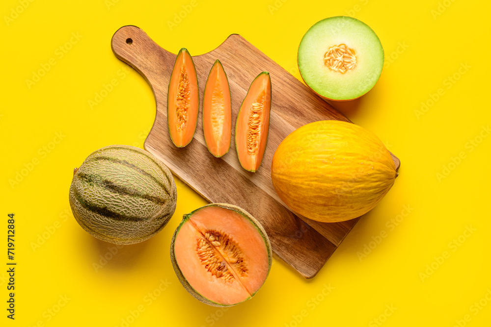 Wooden board with tasty ripe melons on yellow background
