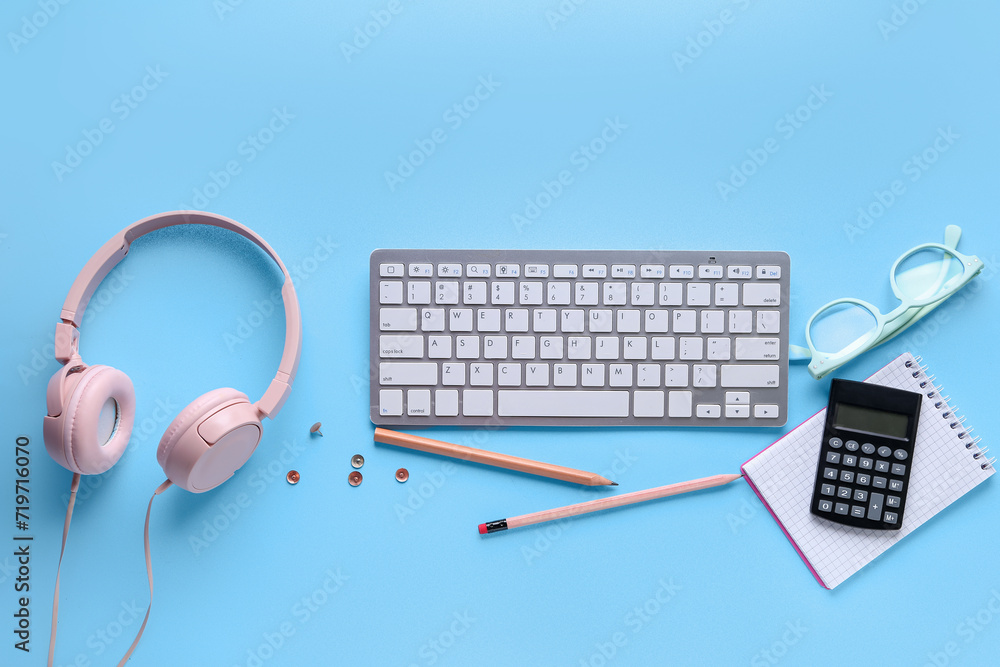 Composition with modern computer keyboard, eyeglasses, headphones and stationery on blue background