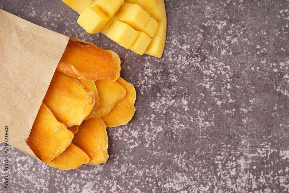 Paper bag with slices of dried mango on dark table