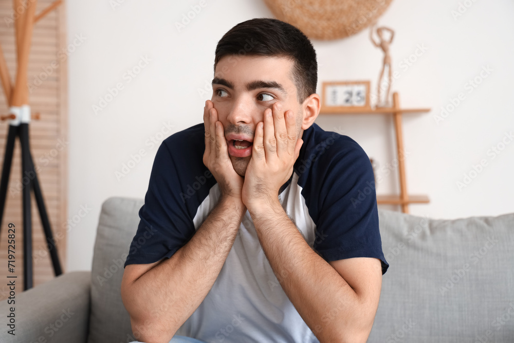 Afraid young man sitting on sofa in living room