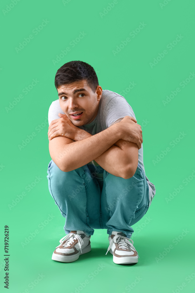 Afraid young man sitting on green background