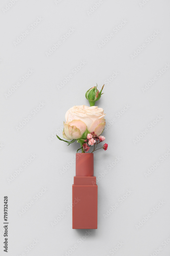 Composition with lipstick and beautiful flowers on grey background