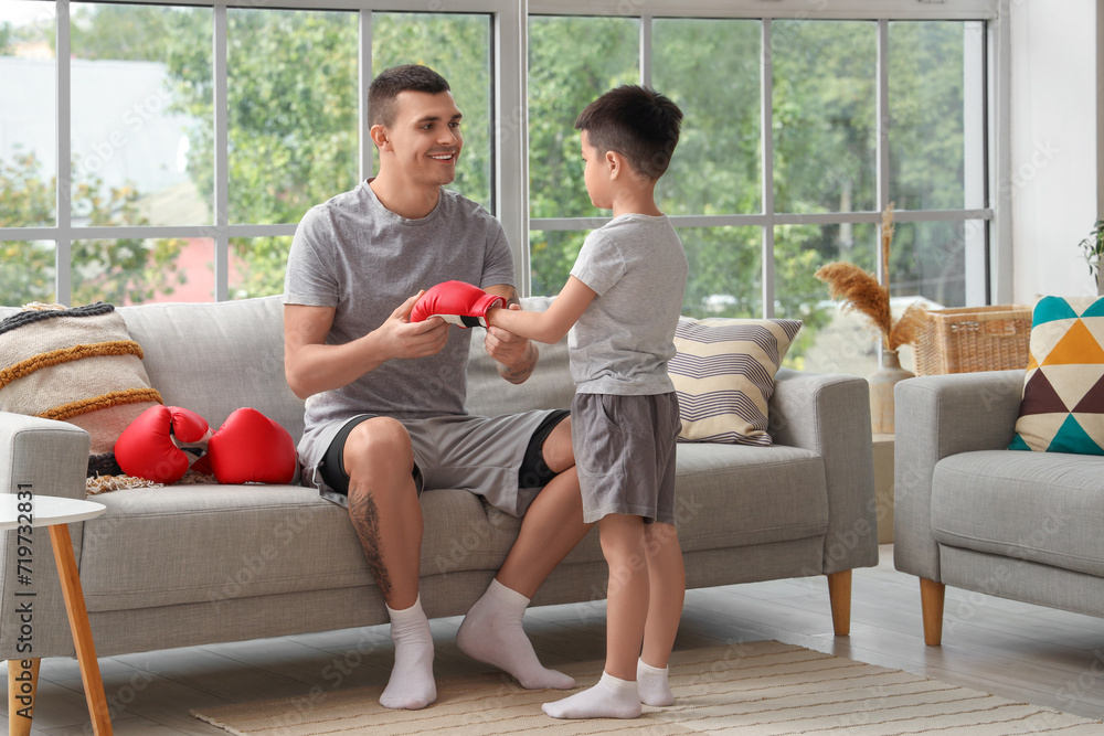 Young man and his little son with boxing glove at home