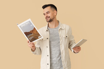 Wall Mural - Handsome man with magazine and tablet computer on beige background