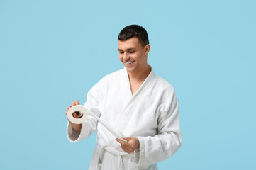 Sticker - Portrait of handsome young man in bathrobe with toilet paper on blue background