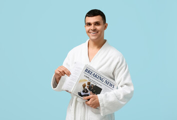 Sticker - Portrait of handsome young man in bathrobe with newspaper on blue background