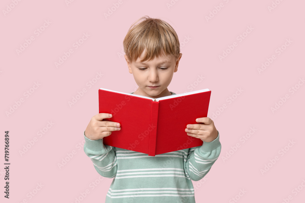 Little boy reading book on pink background