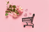 Fototapeta Mapy - Small shopping cart with paper hearts and flowers on pink background. Valentine's Day celebration