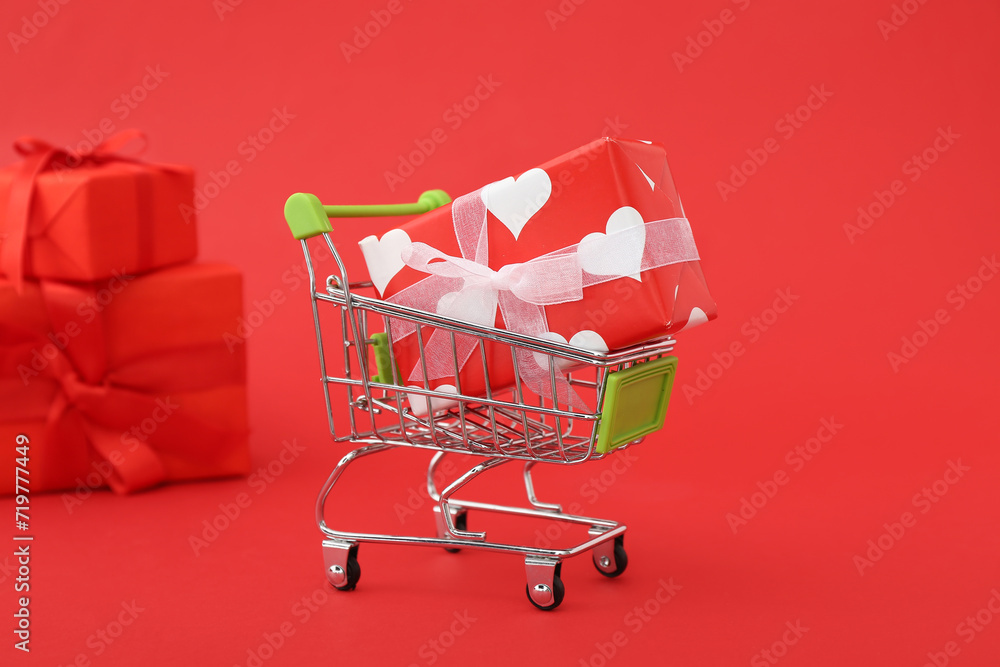 Small shopping cart with gift boxes on red background. Valentine's Day celebration