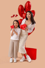 Wall Mural - Young Asian woman and her little daughter holding gift box, paper hearts and air balloons on brown background. Valentine's day celebration