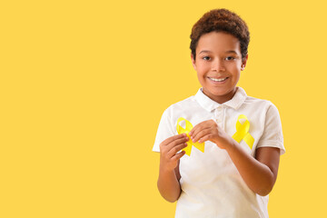 Poster - Cute little African-American boy with yellow ribbons on color background. Childhood cancer awareness concept