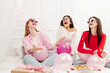 Group of overjoyed beautiful girls, best friends wearing glasses communication, celebration birthday, having fun with confetti and balloons sitting on bed. Holiday, bachelorette party concept
