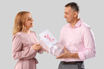 Canvas Print - Middle-aged couple with gift box and greeting card on grey background. International Women's Day