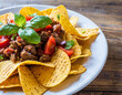 Close-up of nachos, a Mexican dish featuring tortilla chips topped with beef and fresh vegetables, set against a wooden background.