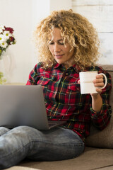 Wall Mural - Beautiful adult young woman at home with laptop computer lay down on the couch - concept of alternative office and workstation - modern job with technology and people -  curly long hair