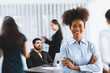 © Summit Art Creations - Young African businesswoman portrait poses confidently with diverse coworkers in busy meeting room in motion blurred background. Multicultural team works together for business success. Concord