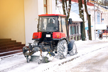 Wall Mural - Tractor with rotating brush clean snow from sidewalk. Heavy duty vehicle with brush and snowplow removing snow from pedestrian zone on road. Tractor clearing . snowy streets with snow plow and brush