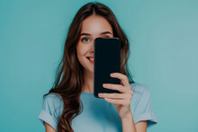 Cheerful Young Woman In A Blue Shirt Peeks Out From Behind A Large Smartphone