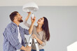 © Studio Romantic - Happy young family couple changing a light bulb together. Cheerful, smiling man and woman standing on a step ladder at home and placing a modern energy saving lightbulb in a white lamp on the ceiling
