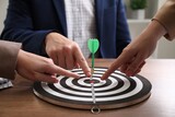 Fototapeta  - Business targeting concept. People pointing at dartboard at wooden table indoors, closeup