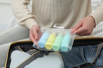 Woman with plastic bag of cosmetic travel kit packing suitcase, closeup. Bath accessories