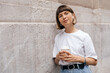 © PhotoBook - Close up portrait of lovely cute girl with short hairstyle is listening music in headphones and holding coffee while posing near the wall